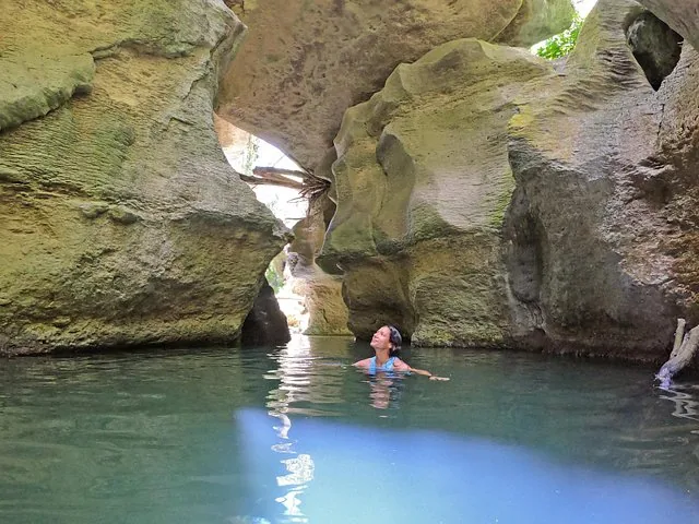 Woman swimming in clear blue water surrounded by large rocks