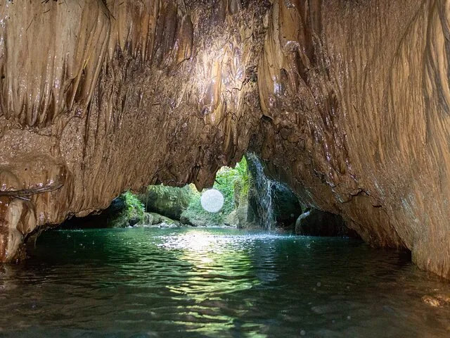 Ingresso della grotta con un fiume che scorre all'interno e una cascata
