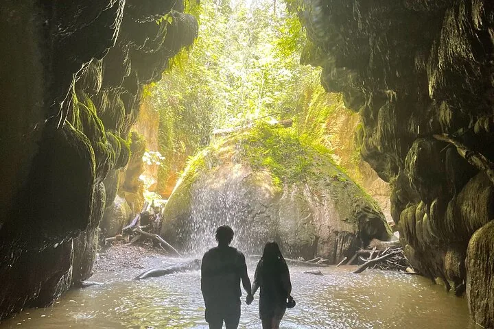 Pareja tomada de la mano frente a una cascada dentro de una cueva